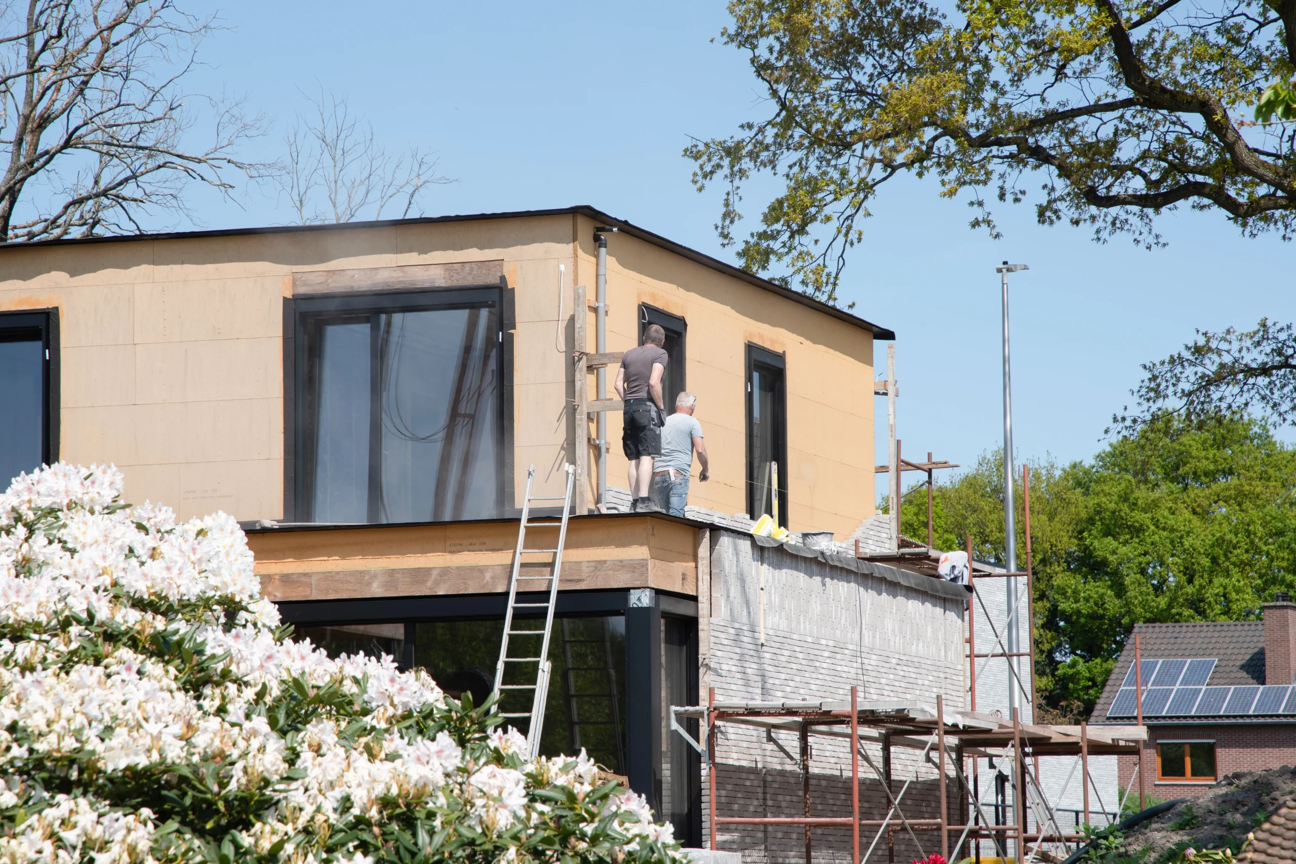 Chantier de rénovation avec deux artisans maçons travaillant sur l'habillage de la façade d'une maison contemporaine à étage