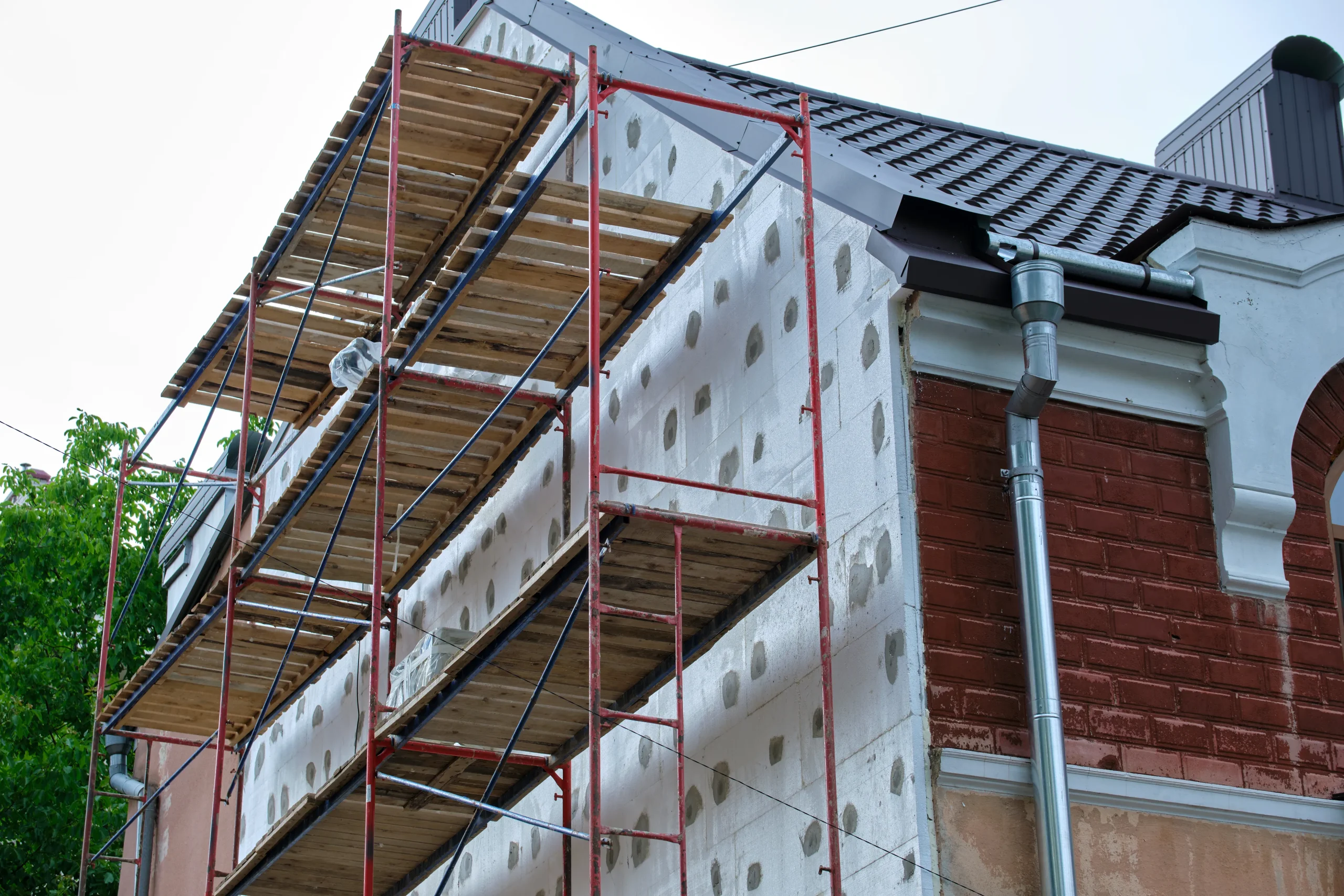 Pose de panneaux isolants de façade (ITE) sous échafaudage pour la rénovation énergétique d'une maison individuelle.