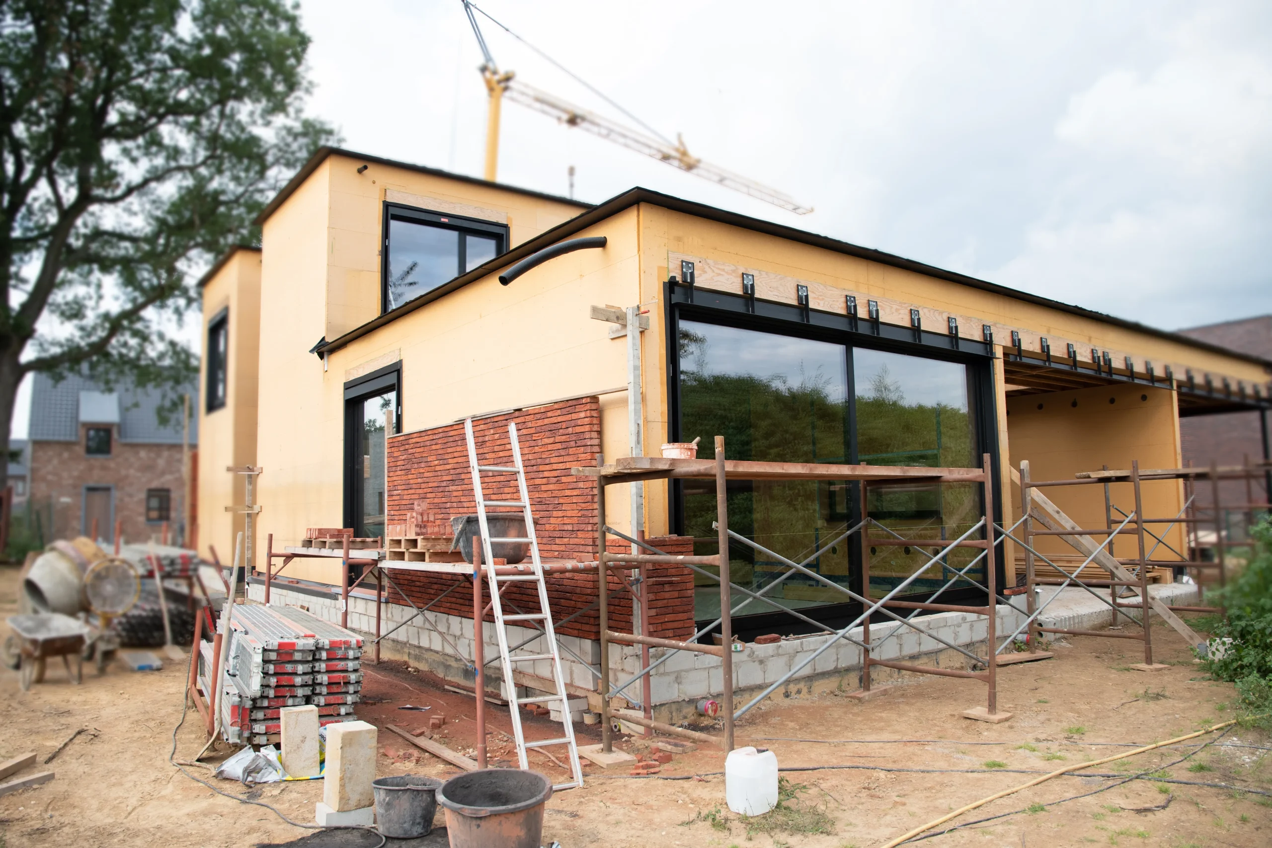 Construction de maison individuelle avec isolation par panneaux d'OSB en cours. Échafaudage et matériel de chantier visibles au premier plan pour le client.