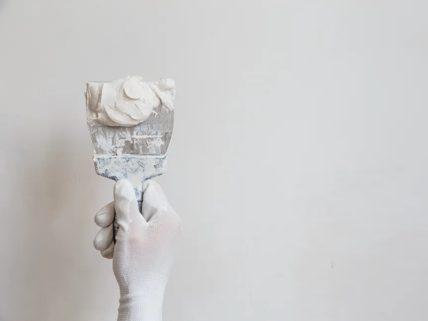 Artisan plâtrier appliquant un enduit de lissage traditionnel sur un mur blanc