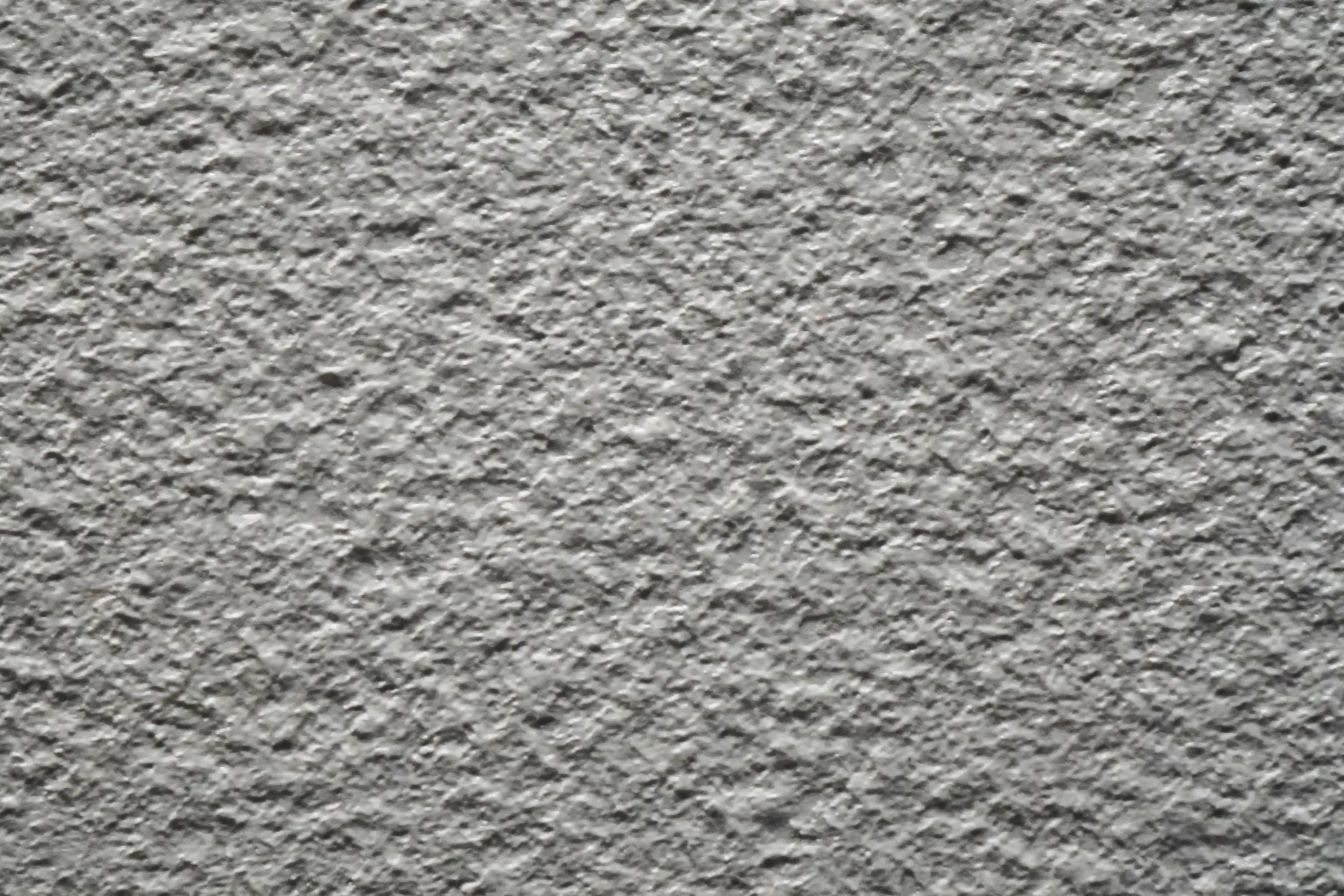 Gros plan sur un enduit de façade gratté de couleur gris clair avec une texture minérale rugueuse et uniforme.