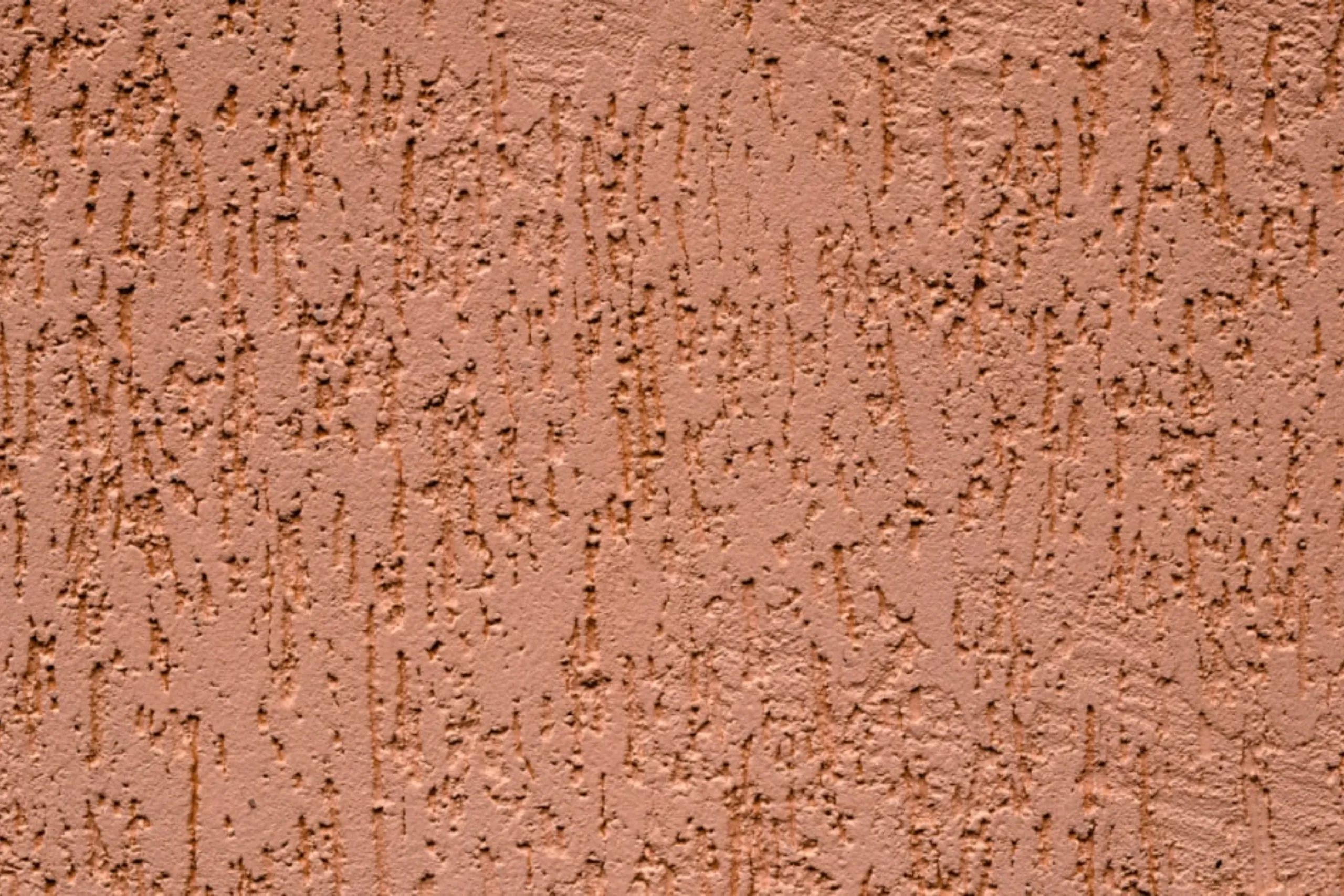 Gros plan sur un enduit de façade écrasé de couleur ocre rosé avec une texture à reliefs lissés et cavités verticales.