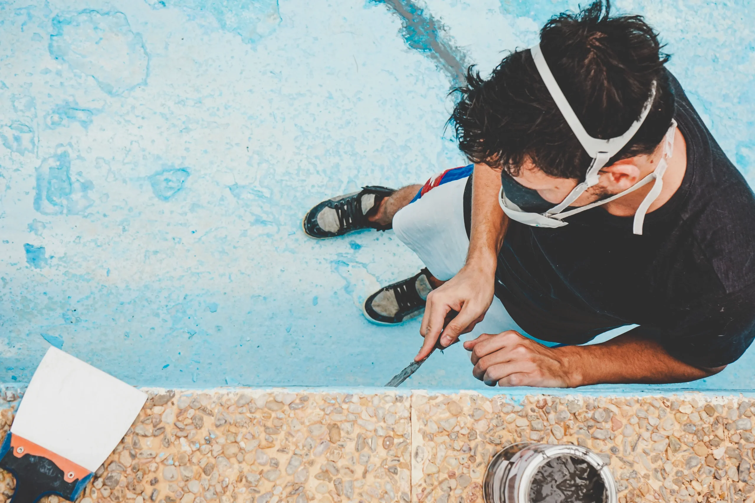 Travaux de rénovation de piscine : préparation et ponçage des parois du bassin bleu par un professionnel.